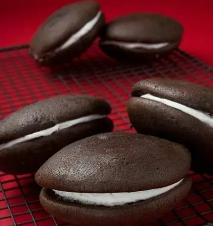 Chocolate whoopie pies with white cream filling on a red cooling rack