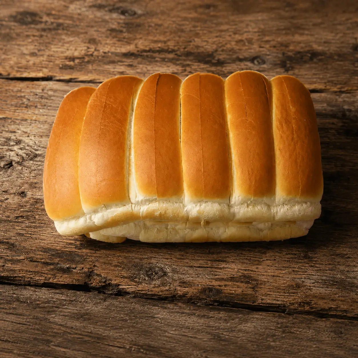 Row of connected New England split-top hot dog rolls on a rustic wooden table