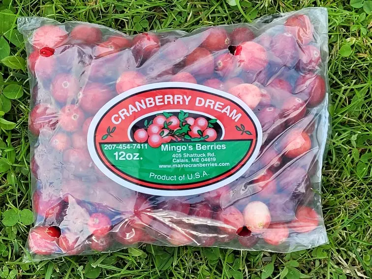 Clear bag of fresh red cranberries labeled Cranberry Dream from Mingo's Berries lying on grass