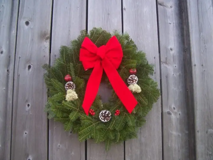 Maine balsam fir holiday wreath with a large red bow and pine cones on a weathered gray wall