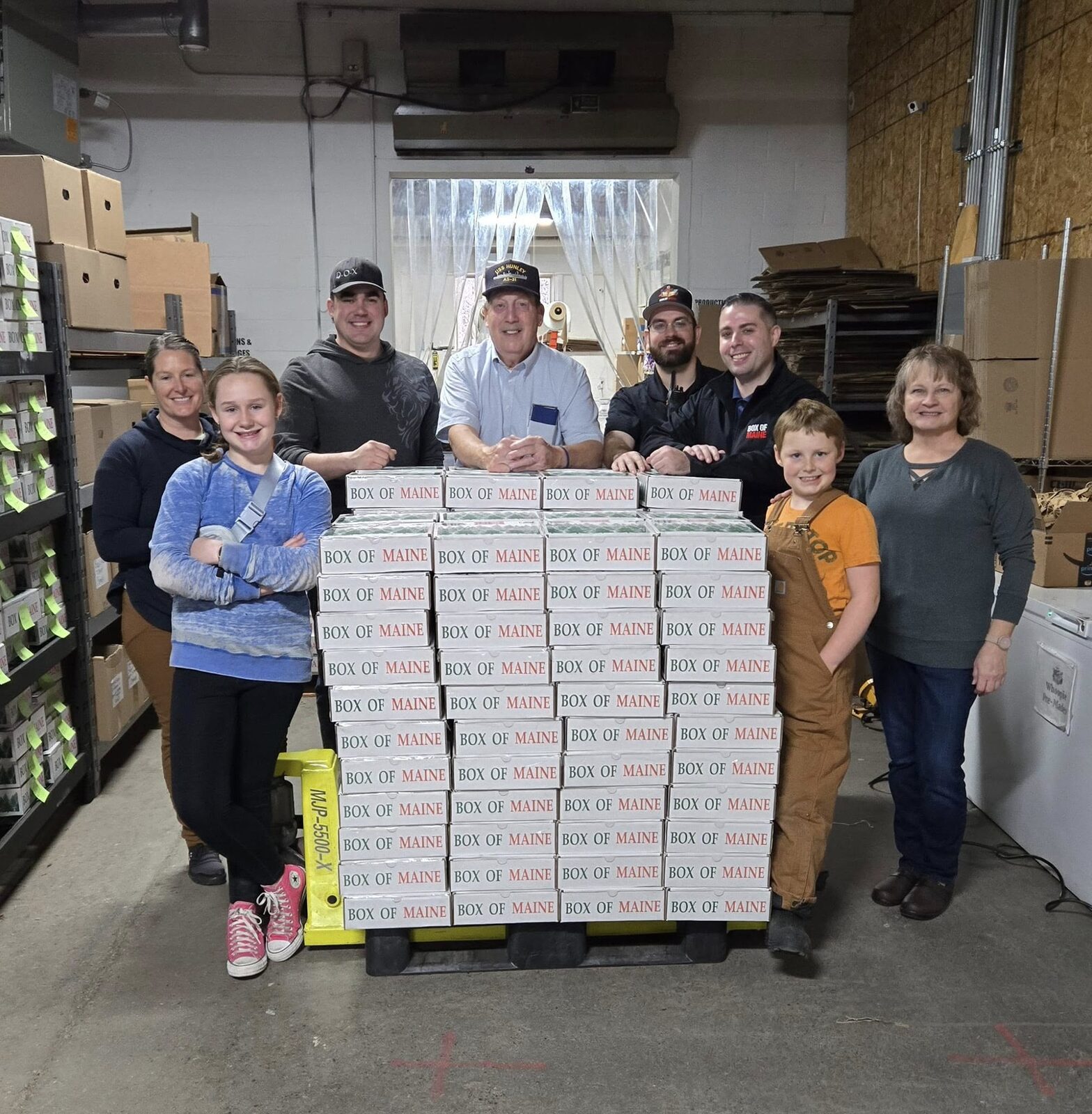 Volunteers and families standing behind a stack of Box of Maine care packages