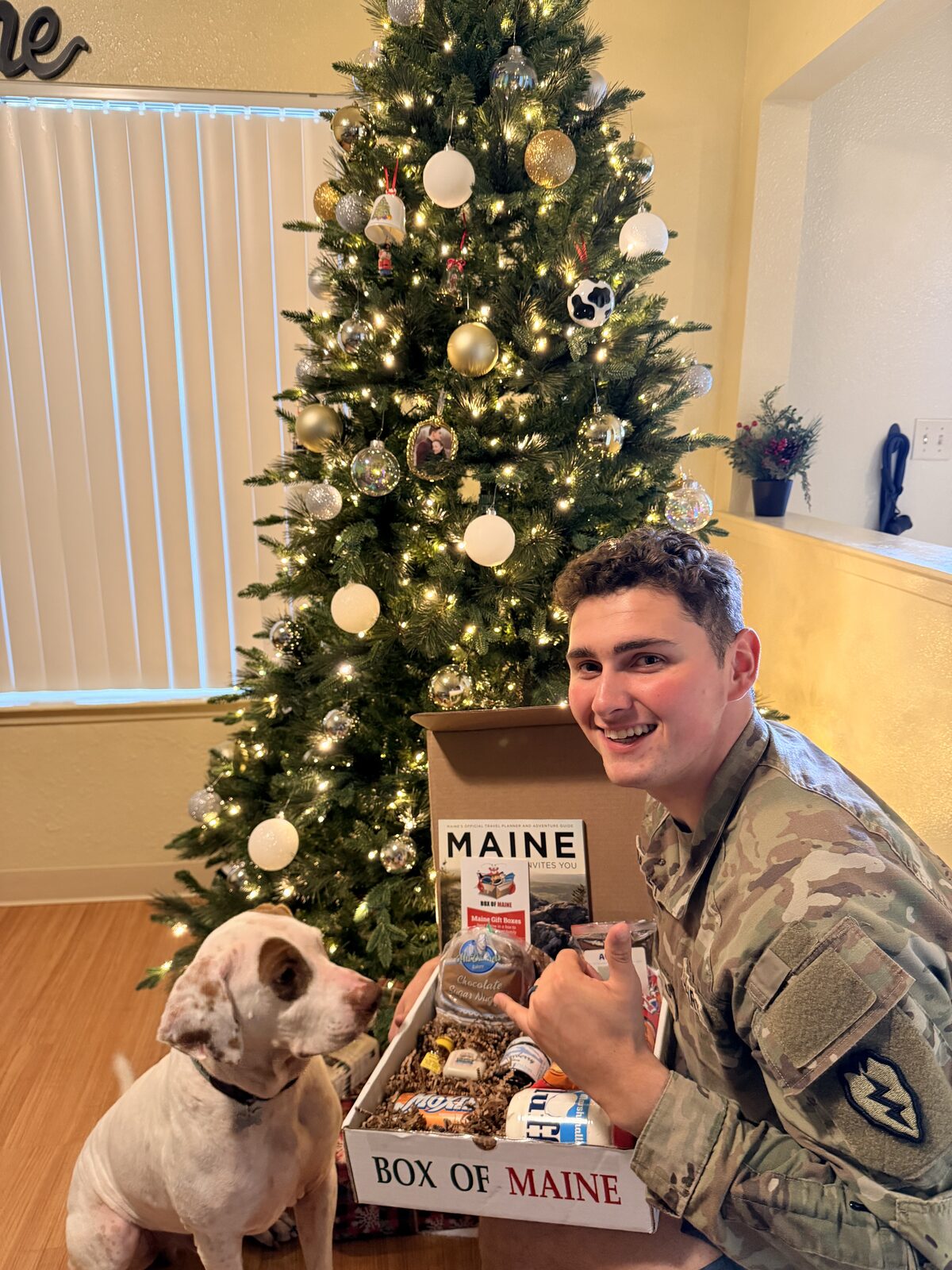 A service member opening a Box of Maine care package beside a Christmas tree